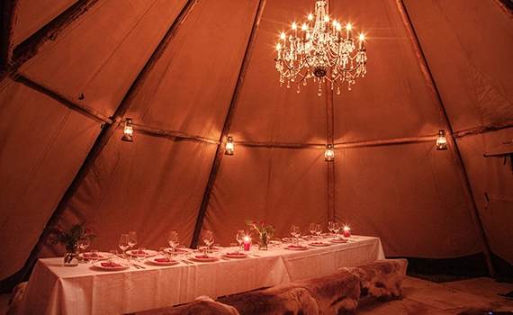 Julebord middagsselskap i Cirrus lavvo i Tentipi stil med lysekrone, bord og stoler med servering.